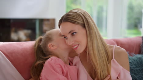 mother talking with daughter at home. girl whispering secret on woman ear
