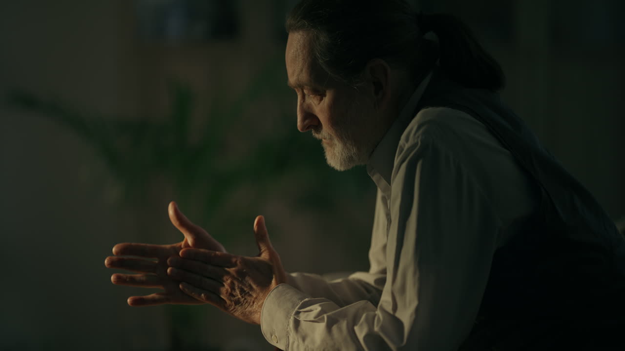 Thoughtful Senior Man with Clasped Hands in Low Light
