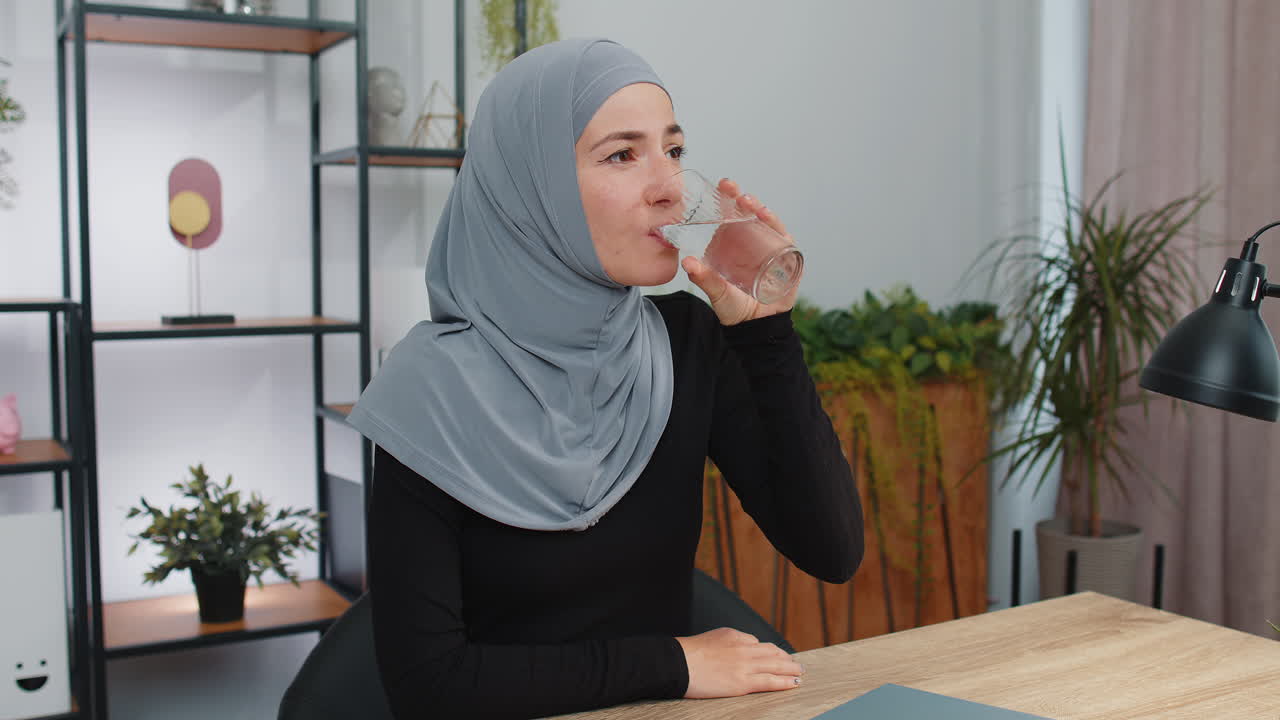 Thirsty muslim woman sitting at home holding glass of natural aqua make ...