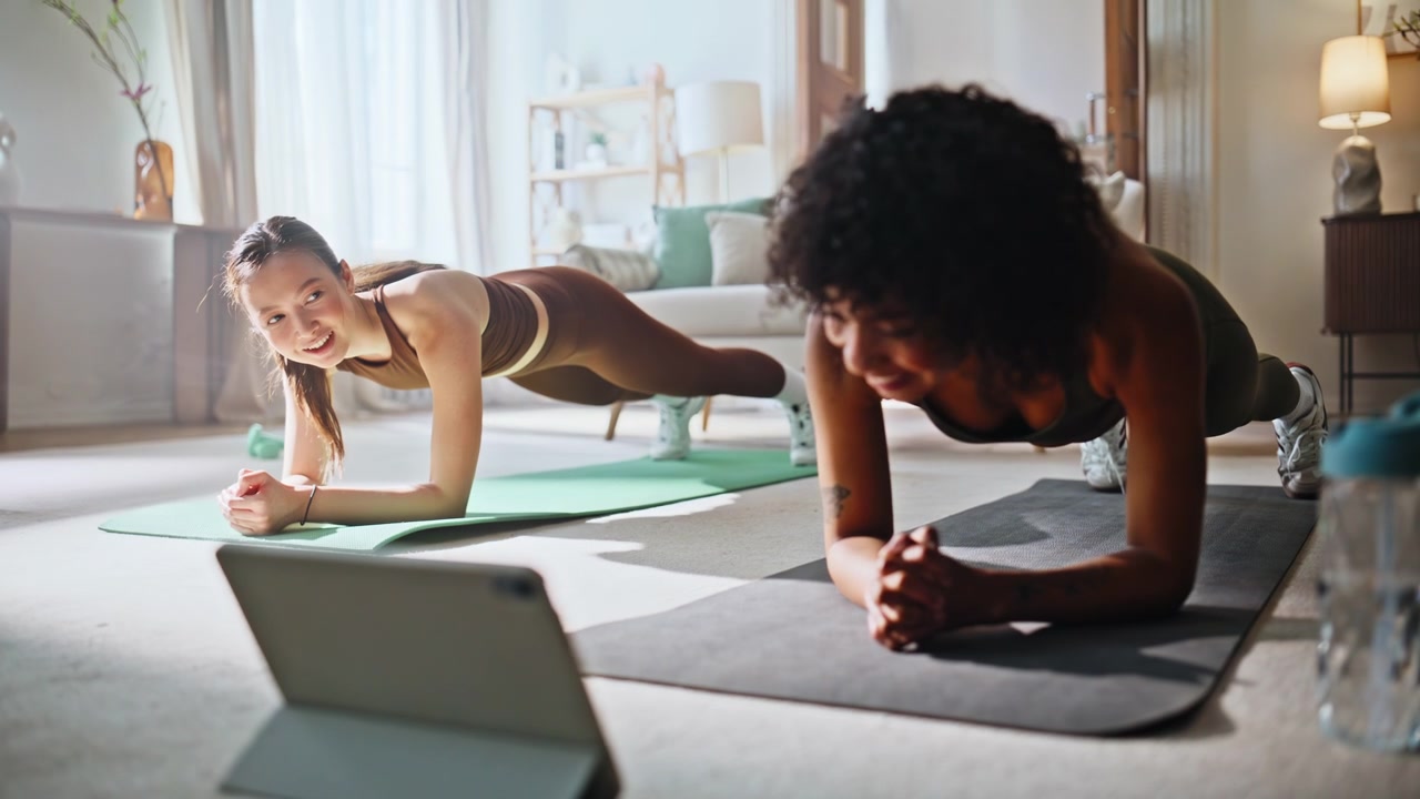 Fitness friends holding plank pose home. Multiethnic women workout indoor.