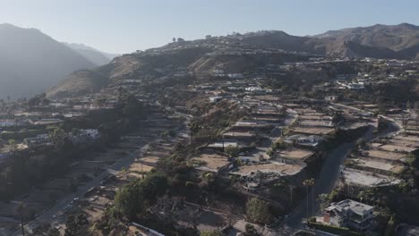 Aerial drone footage flying over the hills of Pacific Palisades, California, showing charred land, damaged homes, and active rebuilding after recent wildfires impacted the residential area