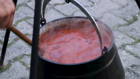 cooking stew in the open air and chef mixes with a wooden mixing spoon, croatia, cobanac, traditional meal, slavonija