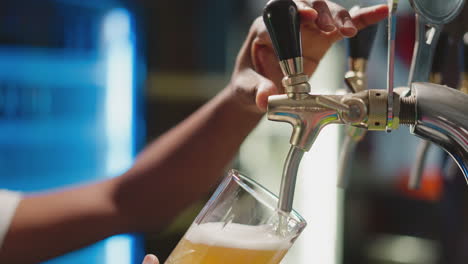 barman fills mug with foamy beer from tap closeup. african american brewery worker pours fresh beverage into glass for guests. man serves craft beer