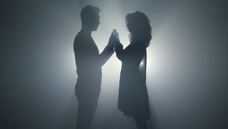 Silhouette-man-woman-standing-in-dark.-Loving-couple-holding-hands-indoors.