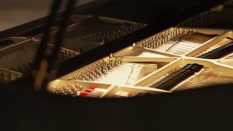 Inside-of-classic-grand-piano-interior-showing-strings,-hammers-and-other-structures-in-close-up.-Complex-wooden-parts-of-a-vintage-instrument-design.-Perfect-black-glossy-paint-shines-in-stage-lights