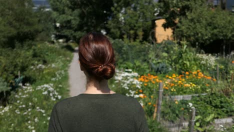 woman walking flower garden path slowly, peaceful walk, back view