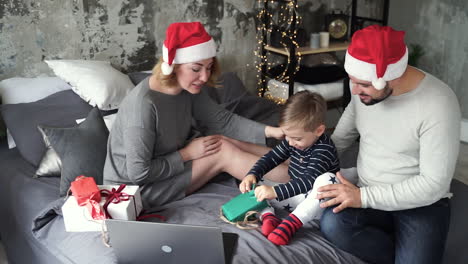 madre, padre e hijo pequeño haciendo videollamadas con su familia y abriendo sus regalos de navidad