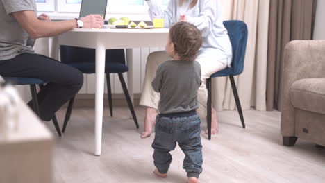 parents sitting at a table and their baby is near a toy box