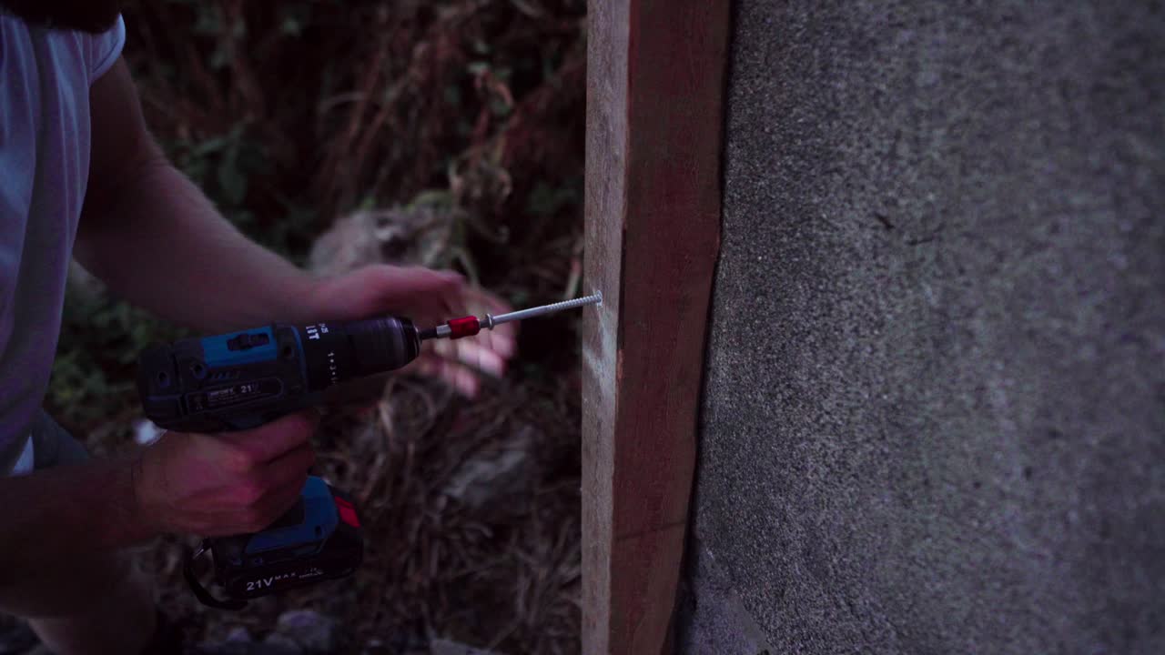 A Man is Using a Drill to Insert a Nail into Wood Intended for the Construction of a Greenhouse in Indre Fosen, Norway - Close Up