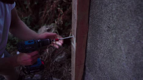 a man is using a drill to insert a nail into wood intended for the construction of a greenhouse in indre fosen, norway - close up