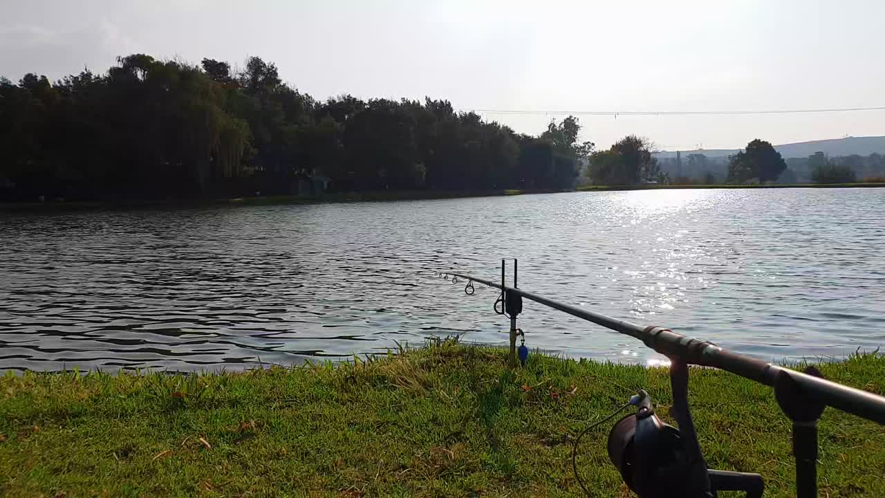 Sebuah joran pancing menunggu umpan dengan matahari terbenam di atas danau yang tenang di kejauhan