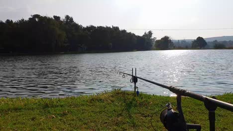 a fishing rod waiting for a bite with the sun setting over a calm lake in the distance