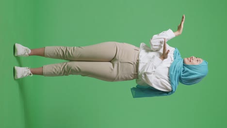 full body of asian muslim woman smiling and pointing to side while standing in the green screen background studio