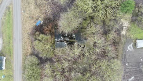 Slow-zoom-in-on-abandoned-house-farm-collapsed-and-damaged-roof-near-trees