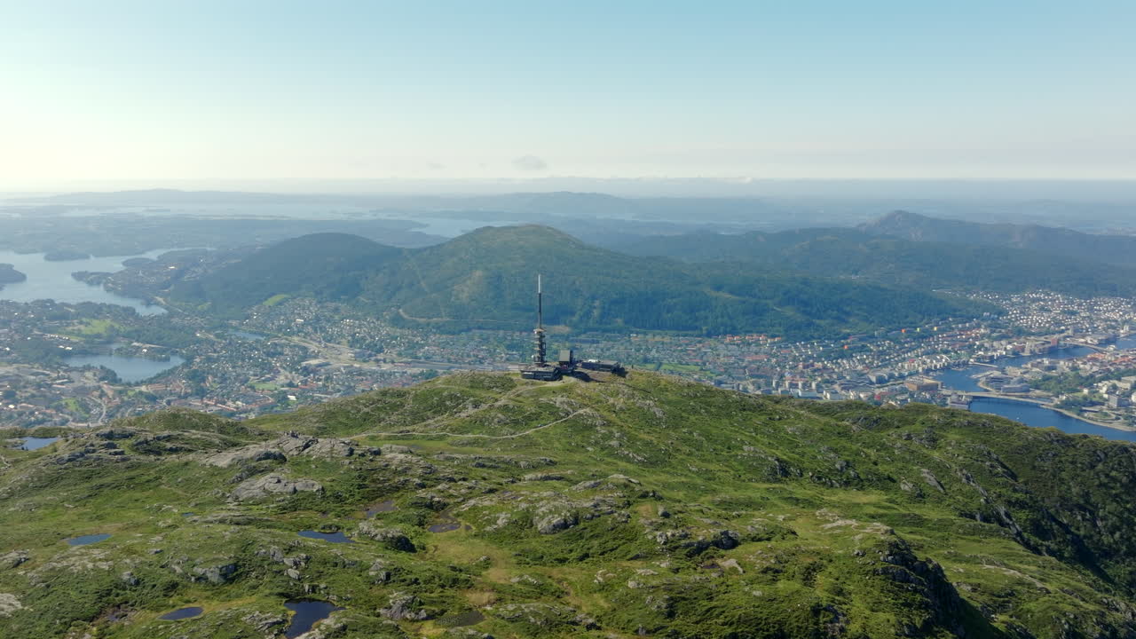 Aerial footage circling Ulriken on a sunny summer day, capturing panoramic mountain, fjord and city views over Bergen