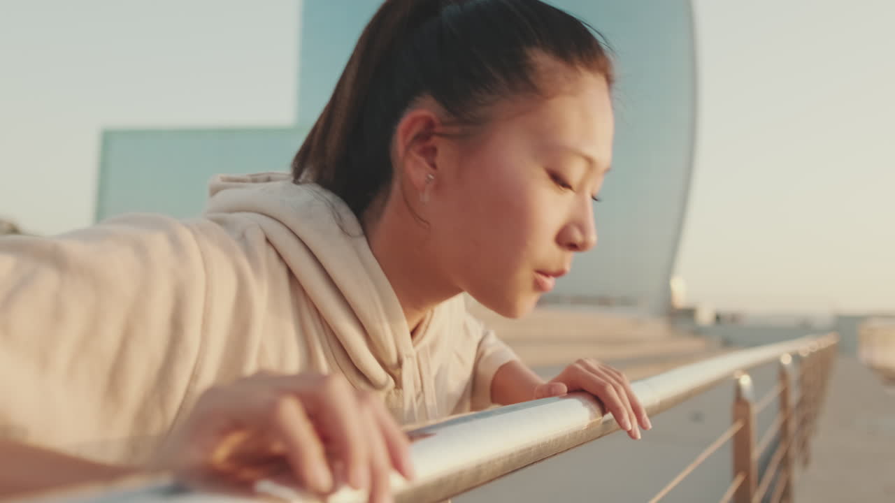 Asian woman wearing a hoodie looking out at buildings from a balcony