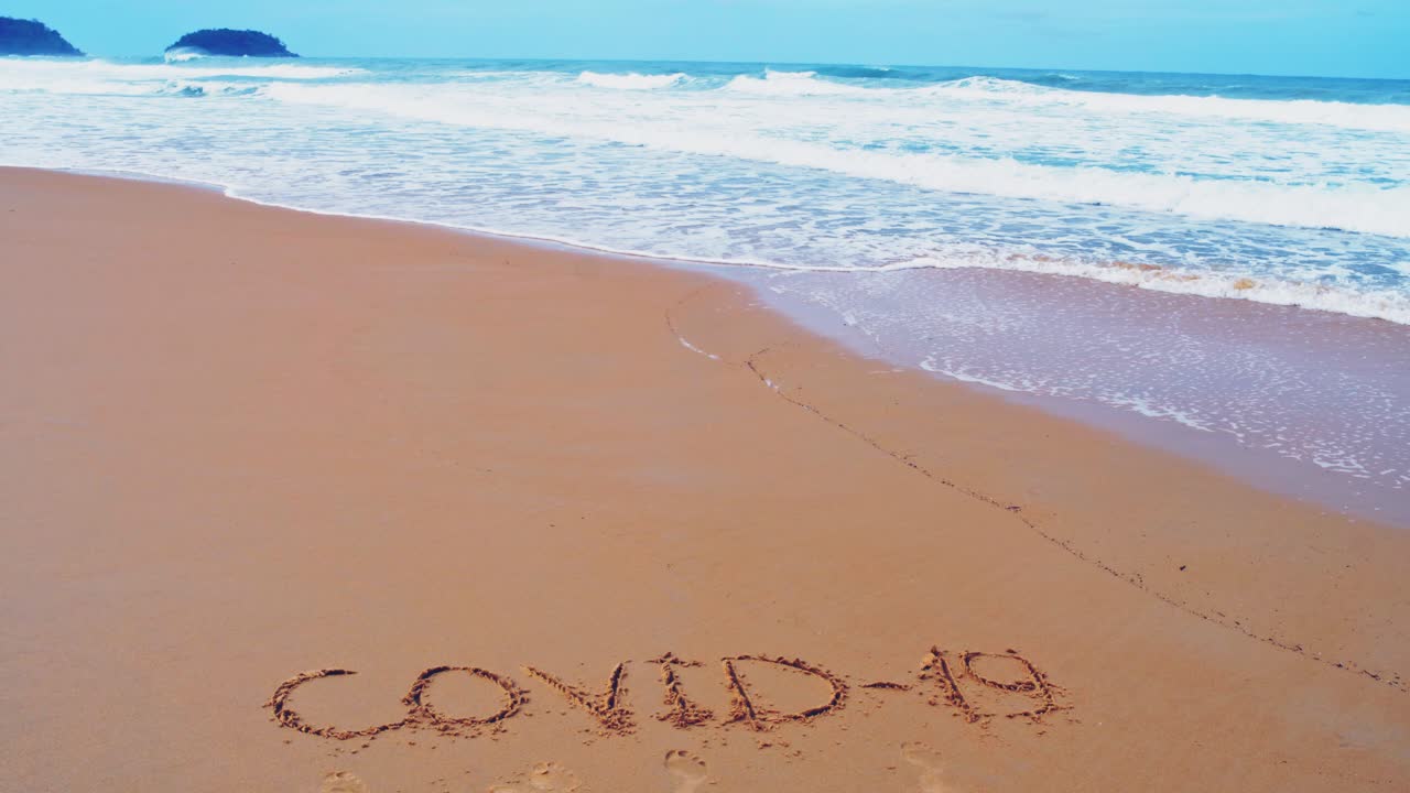 바다 해변에서 covid-19라는 문자를 보내고 잠금 시간 동안 자연 개념의 슬로우 모션 파동으로 모래에 파도를 튀깁니다.