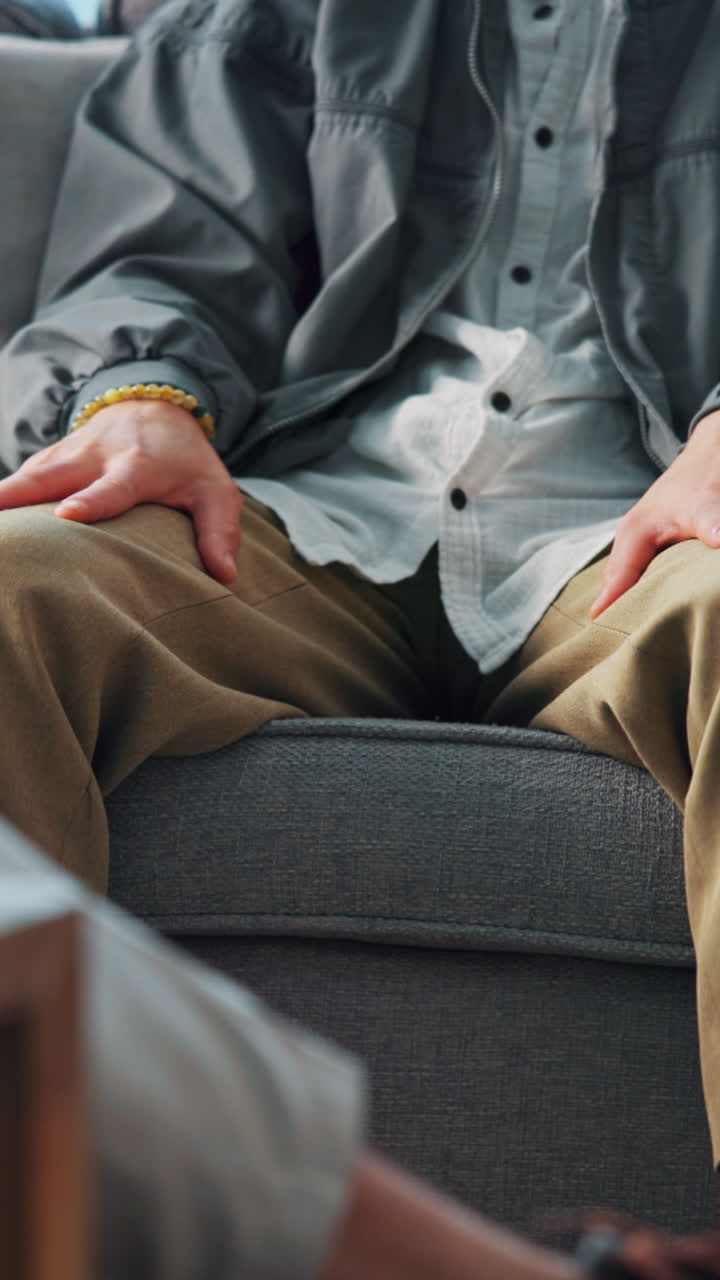 Nærbillede af person, der sidder afslappet i en sofa med hænderne på knæene
