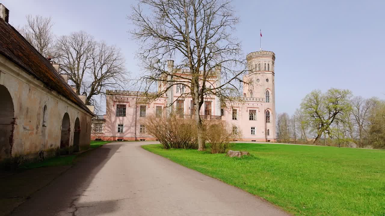 Peaceful forward drone flight revealing pink Vecauce Castle on sunny calm day