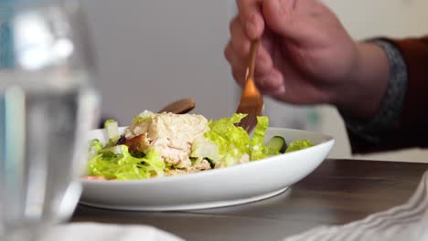 man sitting at table in a restaurant eating salad of vegetables and chicken