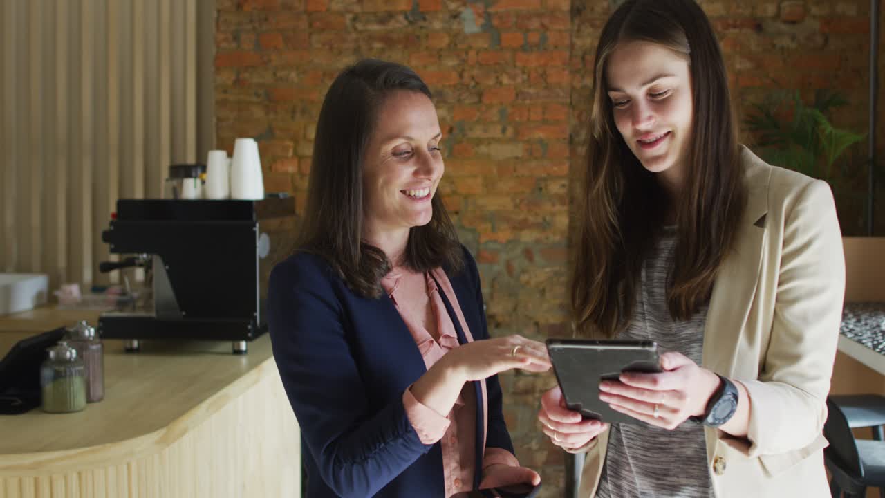 propietaria de un negocio caucásica y su compañera de trabajo usando una tableta y hablando