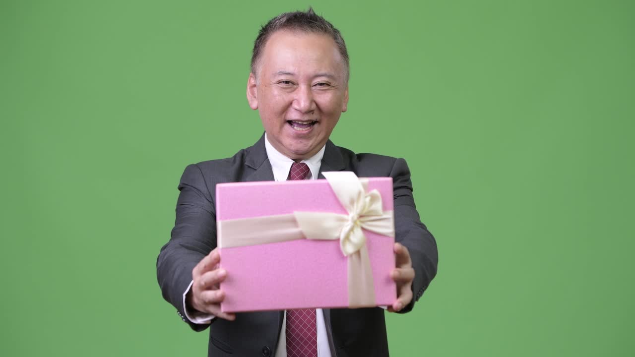 초록색 배경 에 선물 상자 를 가진 성숙 한 일본인 사업가