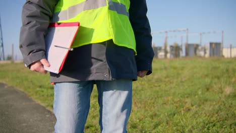 Ingeniero-Masculino-Caminando-Solo-Por-La-Carretera-Mientras-Lleva-Portapapeles,-Toma-De-Seguimiento-Manual