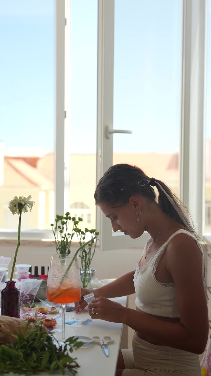 Joven mujer haciendo manualidades en una mesa junto a una ventana soleada.