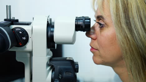 doctor looking into optical device. profile view of a woman ophthalmologist testing eyesight through the medical apparatus in clinic.