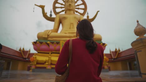 girl walking on steps up to golden big buddha statue in temple