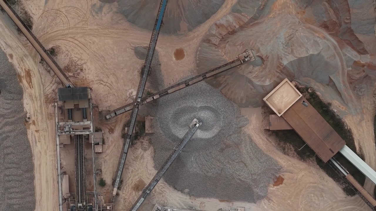 An aerial drone view captures the vast operations of an industrial gravel and sand quarry, showcasing heavy machinery processing raw materials for construction.