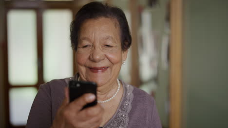 portrait of elderly woman using smartphone enjoying reading online messages senior mixed race woman watching video on mobile phone laughing happy in retirement home