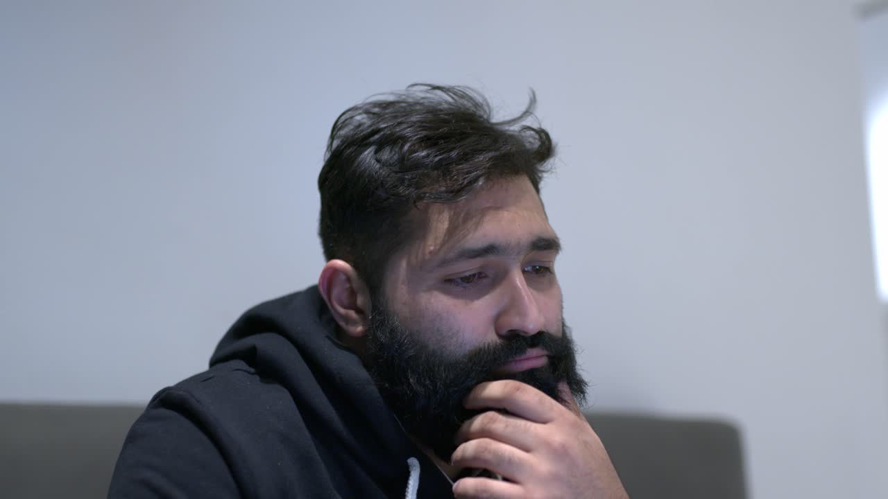 un hombre que sufre de aburrimiento mirando hacia abajo y frotándose la barbilla