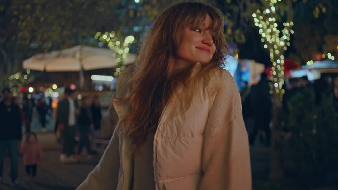 크리스마스 마켓 밤에 춤을 추는 여성은 축제 조명으로 둘러싸여 있습니다.