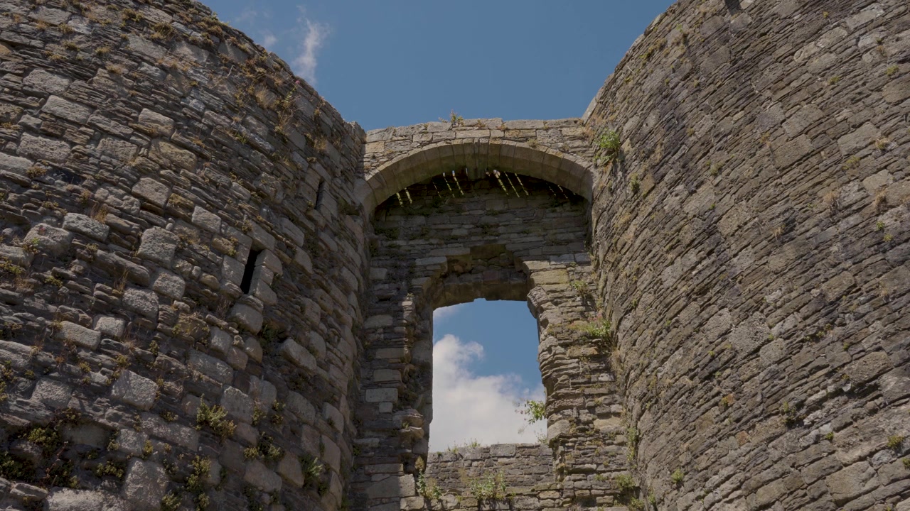 Inquadratura fissa che si concentra su un portale in pietra all'interno del Castello di Beaumaris, rivelando la pesante muratura medievale, le texture della pietra invecchiata e i dettagli architettonici che circondano l'ingresso storico