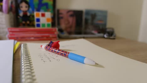 Static-shot-of-a-Spiderman-pen-atop-a-notebook-with-Japanese-letters-written-and-other-items-in-the-background