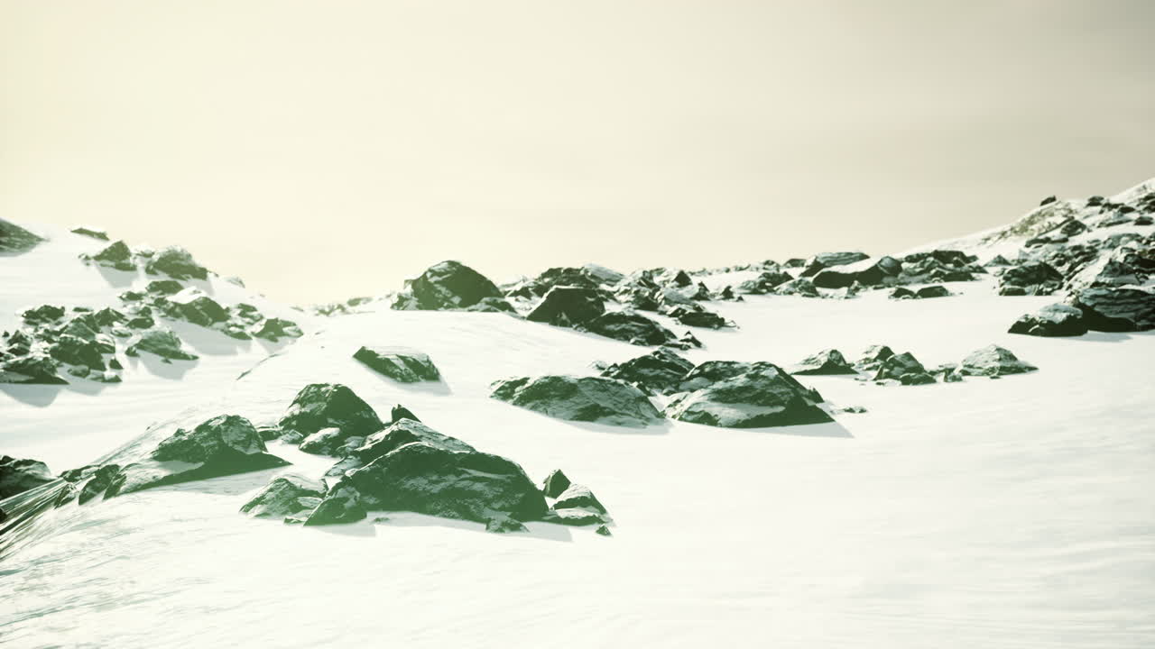 Snowy landscape with boulders and mountainous terrain under soft light