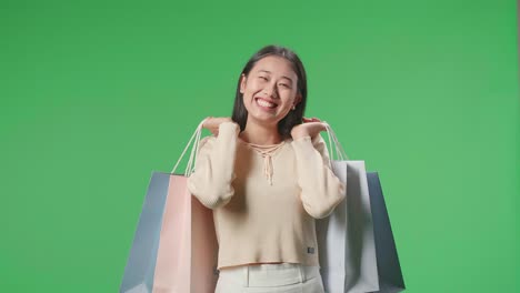 una mujer de compras asiática sosteniendo bolsas de compras siendo feliz y sonriendo a la cámara mientras está de pie frente a la pantalla verde