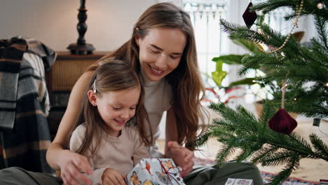 Lächelnde-Frau-Und-Kind-Schütteln-Geschenk-Gemütliches-Haus-Aus-Nächster-Nähe.-Familie-Packt-Geschenke-Aus