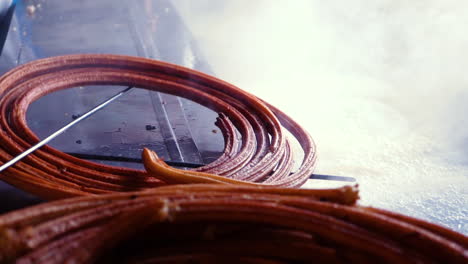 freshly cooked hot churro is pulled out of fryer by a chef in churreria kitchen