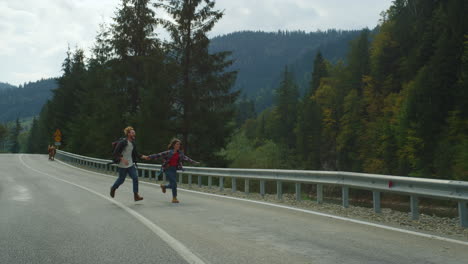 Excursionistas-Corriendo-Por-La-Carretera-De-Las-Montañas-En-Un-Paisaje-Verde.-Mochileros-Felices-Disfrutan-De-Viajar