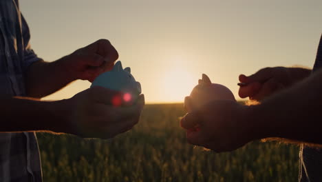 a couple of farmers put money in a piggy bank, stand against the backdrop of a wheat field at sunset. investments and savings in agriculture