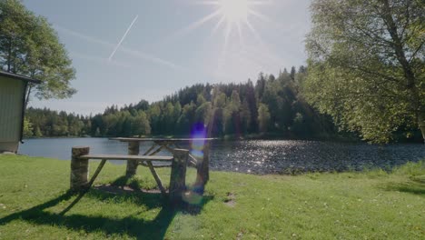 empty wooden bench by kypesjön lake in borås, sweden, wind blowing in the trees, late summer - wide shot static