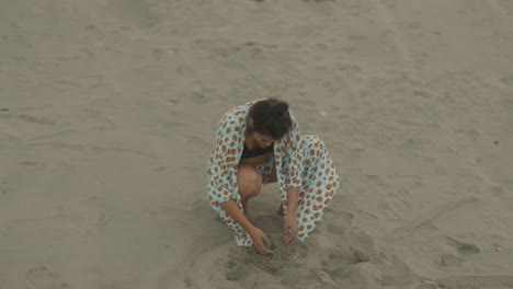 a woman is crouching on the sandy beach, fully immersed in playful exploration