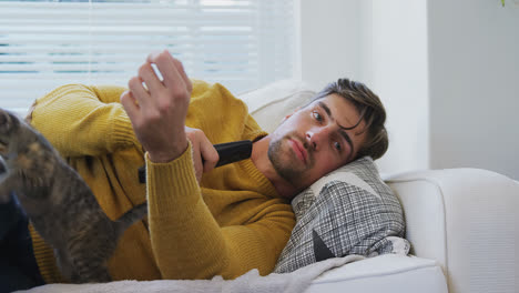 Joven-Tumbado-En-Un-Sofá-Viendo-Televisión-Mientras-Un-Gato-Camina-Sobre-él-4k-4k