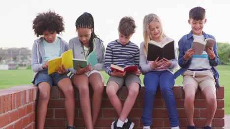 Gruppe-Von-Kindern,-Die-Bücher-Lesen,-Während-Sie-Auf-Einer-Ziegelwand-Sitzen