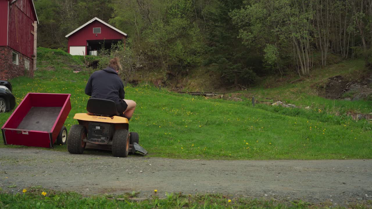 Bagfra af en mand, der kører på en plæneklipper i baghaven