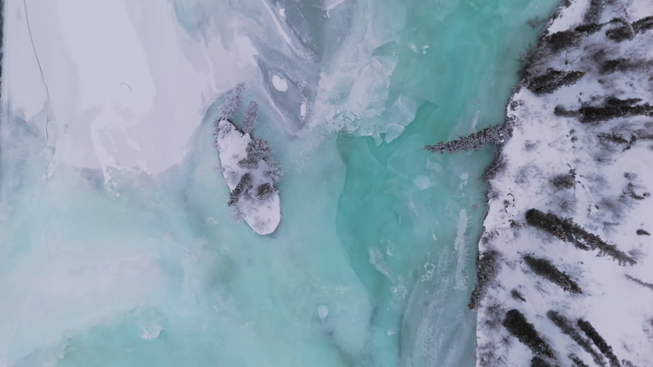 A cinematic pull-out bird’s-eye shot glides over a frozen river and lake, revealing expansive winter scenery. This overhead view highlights the serene, snow-covered landscape and icy waters.