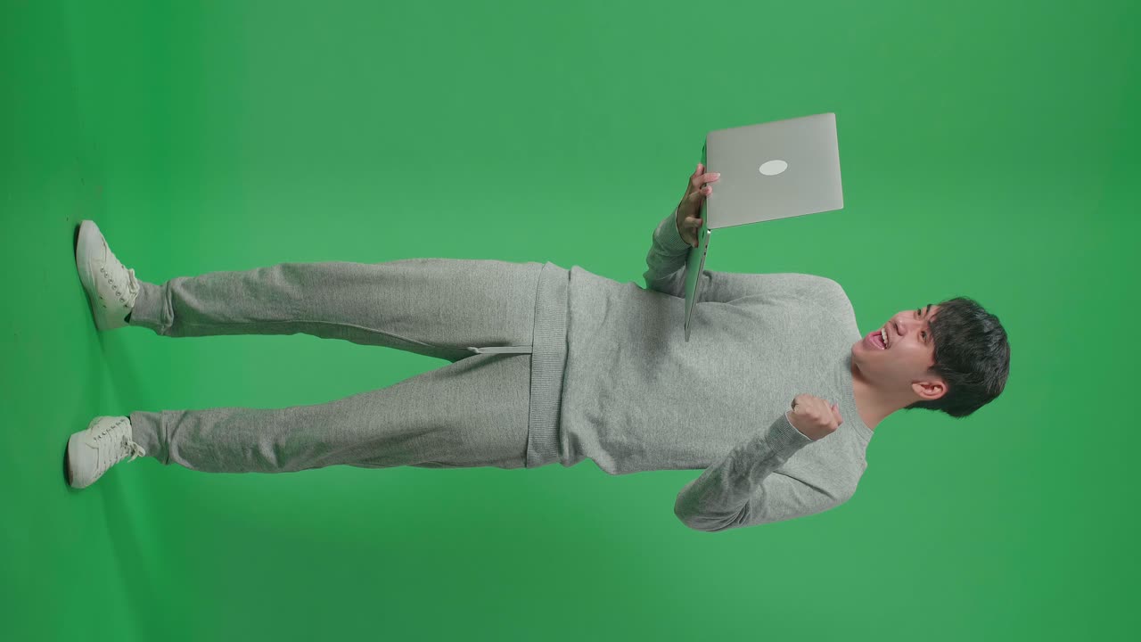 cuerpo lleno de feliz hombre asiático celebrando mientras usa la computadora en el fondo de la pantalla verde
