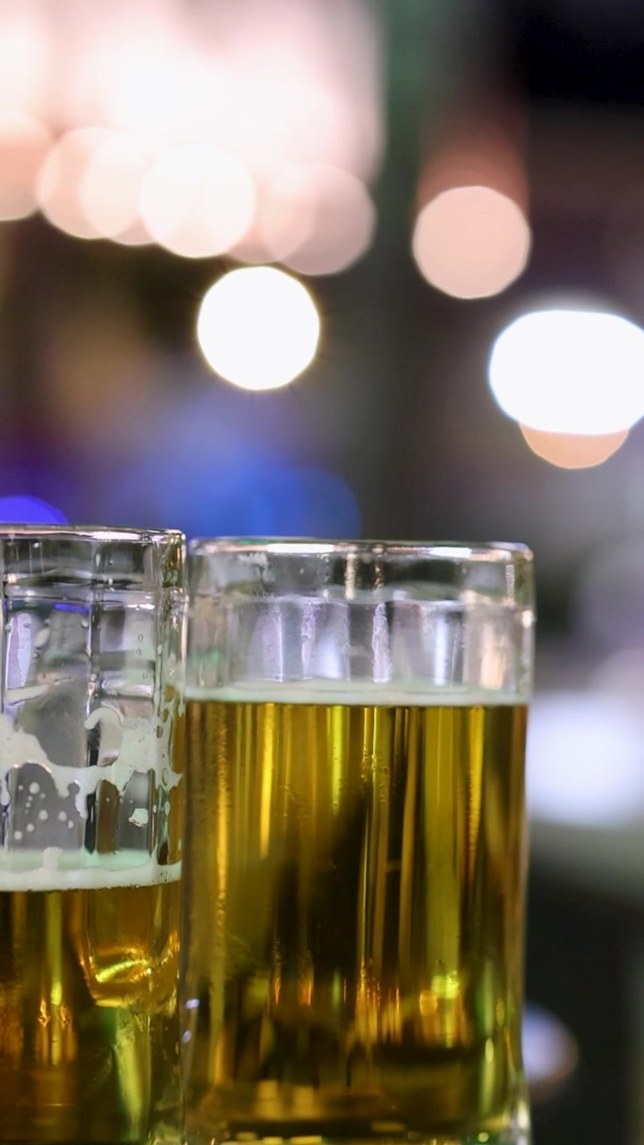Una serie di bicchieri di birra su un bancone da bar con luci vivaci e sfocate della vita notturna sullo sfondo